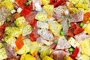 Raw vegetables  potatoes, carrots, green peas, red pepper and onion with pork meat garlic and spices in pyrex tray prepared for