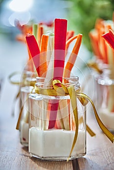 Raw vegetables with sauce in portion glasses on a wooden board, vertical front view. Glasses of assorted fresh raw