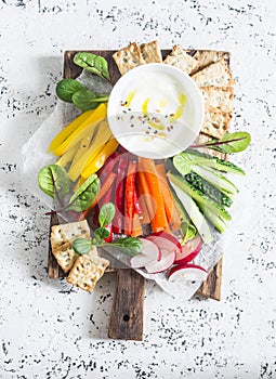 Raw vegetables and yogurt sauce on a wooden cutting board, on a light background, top view. Vegetarian healthy food