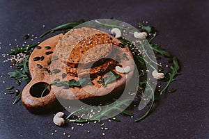 Raw veggie burger on wood and black background with pumpkin seeds, arugula leaves, cashew and sesame seeds. inviting nutritious