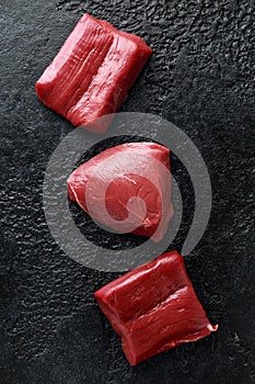 Raw venison steak on black rustic table.