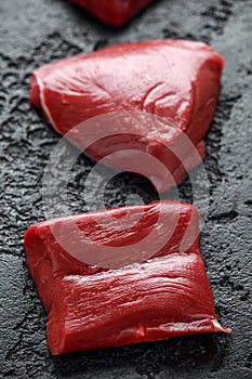 Raw venison steak on black rustic table.