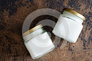 Raw virgin coconut oil in glass jars on abstract wooden background. Top view