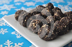 Raw walnut, chocolate and date balls on a white plate and winter background with snowflakes