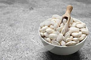 Raw white beans and scoop in bowl on grey table. Space for text