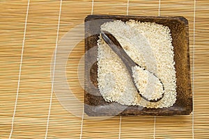 Raw white rice on wooden plate and wooden spoons with rice on bamboo napkin for healthy eating, vegetarianism, top view, flat lay