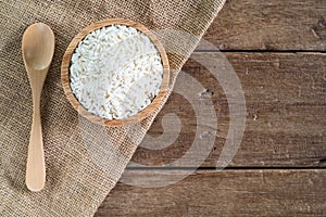 Raw white sticky rice in wood bowl with wood spoon on gunny sack cloth on wooden table