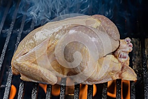 Raw whole chicken on charcoal grill.