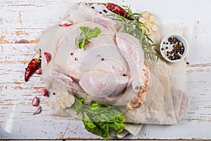 Raw whole chicken with herbs and spices on rustic wood background