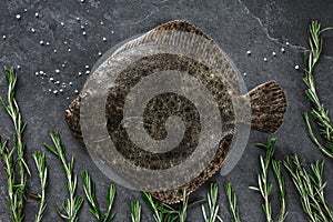 Raw whole flounder fish with rosemary on dark stone background.