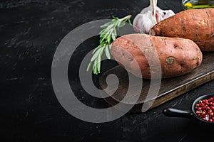 Raw whole sweet potatoe with herbs and spices on black background with copyspace