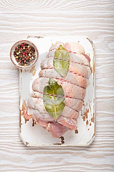 Raw wrapped rolled sliced pork with bay leaf and seasonings on white cutting board on rustic white wooden background top