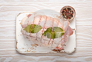 Raw wrapped rolled sliced pork with bay leaf and seasonings on white cutting board on rustic white wooden background top