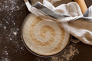 Raw yeast dough resting and rising in large metal bowl covering with linen towel