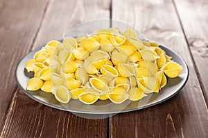 Raw yellow pasta conchiglie on brown wood