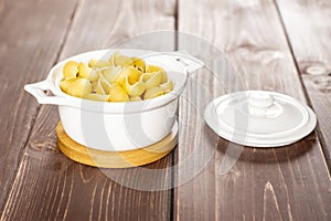 Raw yellow pasta conchiglie on brown wood