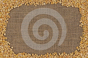 Raw yellow split peas on burlap texture background