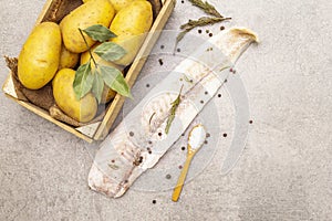 Raw young potatoes and frozen hake fillets. Ingredients for fish and chips. Spices and herbs on a stone background, copy space,