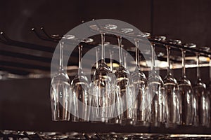 Raws of glasses for a margarita, martini, grog and liqueur hanging upside down in bar at arestaurant, dark background.