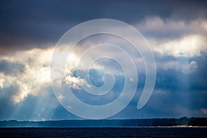 The rays of God in the river landscape. The sun`s rays shine through the clouds over the water surface and the shore