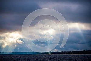 The rays of God in the river landscape. The sun`s rays shine through the clouds over the water surface and the shore. Copy space