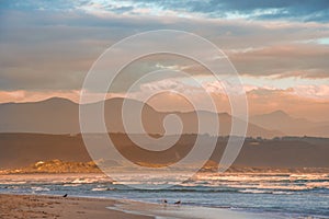 Rays of golden evening light falling on the Plettenberg Bay beach at sunset, with mountains in the distance.