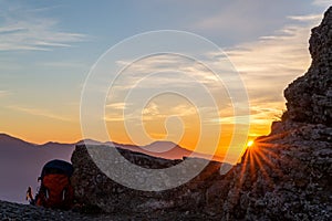 The rays of the setting sun make their way through a piece of rock and a traveler`s backpack