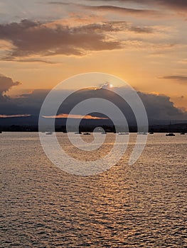 The rays of the sun break out from behind a threatening cloud and illuminate the bay with yachts at sunset in Syracuse.