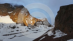 The rays of the sun falling on the summit of the peak. Clouds are visible.
