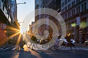 Rays of sunset shine on the diverse crowds of people walking through a busy intersection in New York City