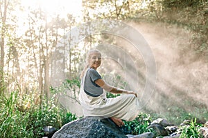 Rays of te sun illuminating a smiling woman sitting on a rock in the rainforest