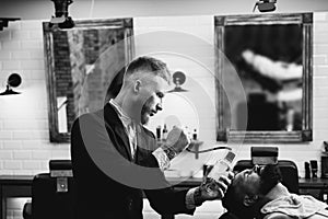 Razor blade. Bearded man getting haircut by hairdresser and sitting in chair at barbershop. Styling with the shaver. Men