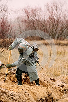 Re-enactor Dressed As German Wehrmacht Infantry Soldier In World War Ii With Shovel Digs Trench. Arrangement Of A