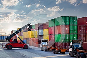 Reach stacker loads container onto truck inside container yard. View of high container stack, heavy machinery.