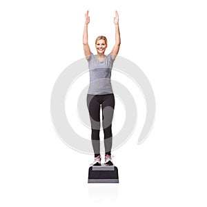 Reaching her fitness goals. A smiling young woman doing aerobics on an aerobic step against a white background.