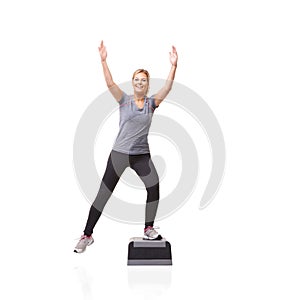 Reaching her fitness goals. A smiling young woman doing aerobics on an aerobic step against a white background - K-step.