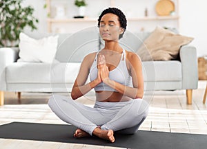 Reaching inner peace and harmony. Positive black woman meditating with closed eyes, doing breathing exercies at home