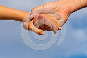 Reaching out hand in hand. A father to his daughter hold hands with a blue sky background