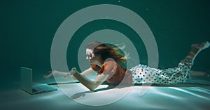 Reaching out to help clients. Young happy determined beautiful business woman dives underwater to use laptop slow motion