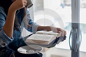 Woman drinking coffee while reading book.