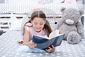 Read fairytale in bed. Girl child lay bed with teddy bear read book. Kid prepare to go to bed. Time for evening