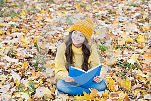Read readily. Happy child read book sitting on autumn leaves. School library. Literacy education. Literature lesson