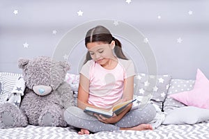 Read before sleep. Girl child sit bed with teddy bear read book. Kid prepare to go to bed. Pleasant time in cozy bedroom