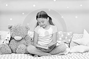 Read before sleep. Girl child sit bed with teddy bear read book. Kid prepare to go to bed. Pleasant time in cozy bedroom