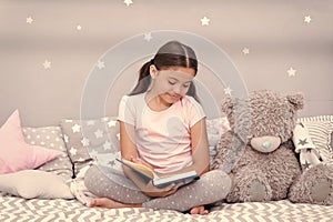 Read before sleep. Girl child sit bed with teddy bear read book. Kid prepare to go to bed. Pleasant time in cozy bedroom