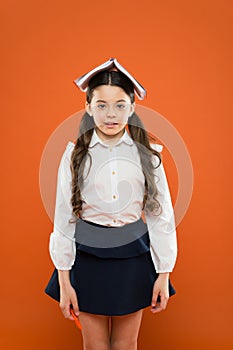 Read a ton, learning is fun. Funny small child holding book to read on her head on orange background. Adorable little