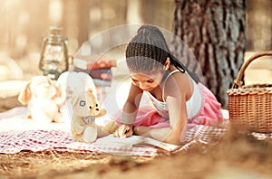 Reading allows kids to explore new worlds. a little girl reading a book with her toys in the woods.