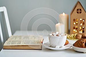 Reading book on cozy winter evening with candles. Christmas light gray background with copy space.