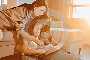 Reading book together. Female lesbian couple with little daughter spending time together at home