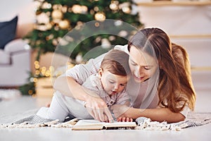 Reading book together. Mother with her little daughter is indoors at home together